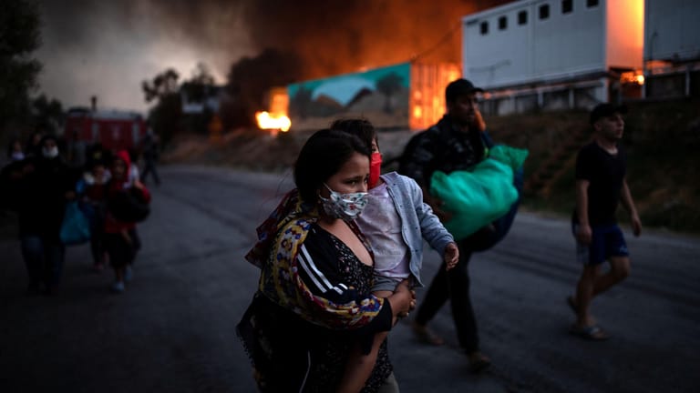 Eine Frau trägt ihr Kind aus dem Feuer in Moria: Seit dem Brand sind die Geflüchteten in einem provisorischen Lager untergebracht.