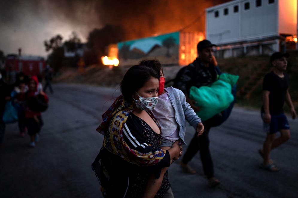 Eine Frau trägt ihr Kind aus dem Feuer in Moria: Seit dem Brand sind die Geflüchteten in einem provisorischen Lager untergebracht.