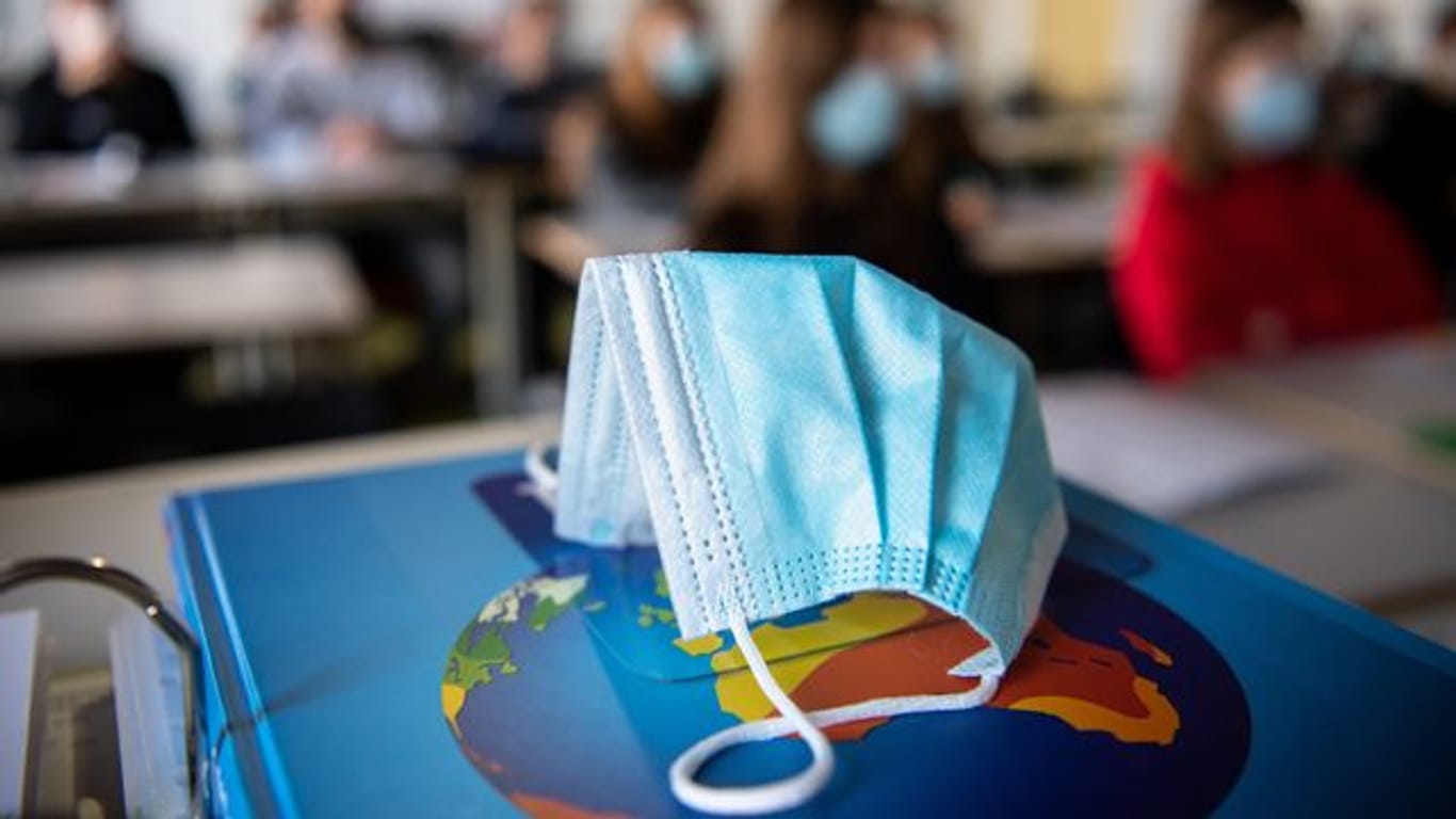 Ein Mund-Nasen-Schutz liegt während des Unterrichts auf einem Atlas (Symbolbild): Im Unterricht und im Schulgebäude müssen Schüler in Berlin nun medizinische Masken tragen.