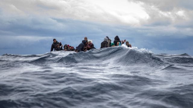Männer aus Marokko und Bangladesch sitzen in einem überfüllten Holzboot im Mittelmeer vor der Küste Libyens, als sich ihnen Helfer der spanischen Organisation "Open Arms" nähern (Archiv). Männer aus Marokko und Bangladesch sitzen in einem überfüllten Holzboot im Mittelmeer vor der Küste Libyens, als sich ihnen Helfer der spanischen Organisation "Open Arms" nähern (Archiv).