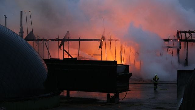 Ein Feuerwehrmann geht in Richtung einer brennenden Lagerhalle