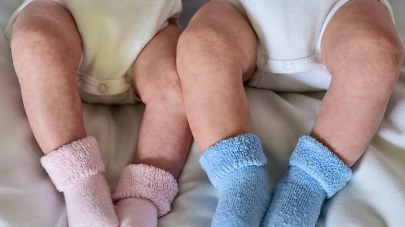 Rosa und blaue Söckchen für ein Mädchen und einen Jungen und die nackten Babybeine von Zwillingen.