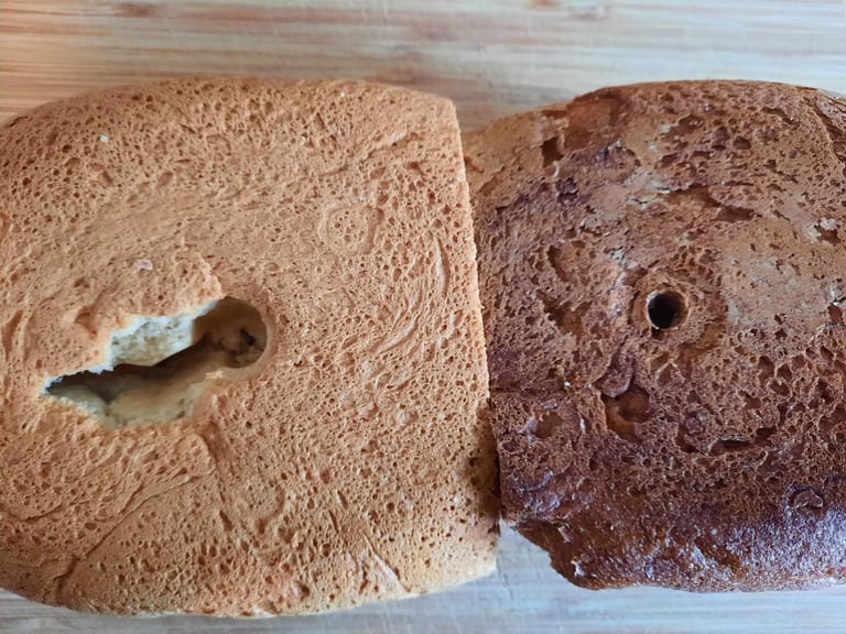 Links das Bauernweißbrot aus unserem ersten Versuch mit dem Loch vom Knethaken. Rechts das Dinkelvollkornbrot aus dem zweiten Durchlauf, bei dem wir den Knethaken zwischendurch entfernt haben.