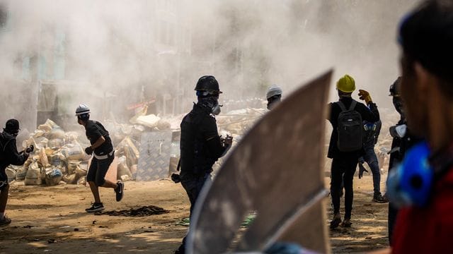 Demonstranten stehen vor rauchenden Trümmern einer provisorischen Barrikade bei einem Anti-Putsch-Protest in Yangon. Demonstranten stehen vor rauchenden Trümmern einer provisorischen Barrikade bei einem Anti-Putsch-Protest in Yangon.