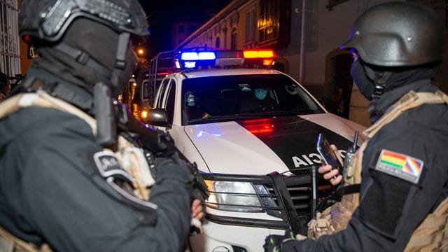 Schwerbewaffnete Polizisten bewachen zwei ehemalige Minister auf ihrem Weg zur Aussage.