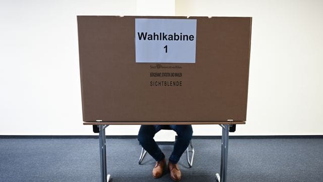 Ein Mann sitzt im Wahlraum des Briefwahllokals Frankfurt Innenstadt hinter einer Wahlkabine.