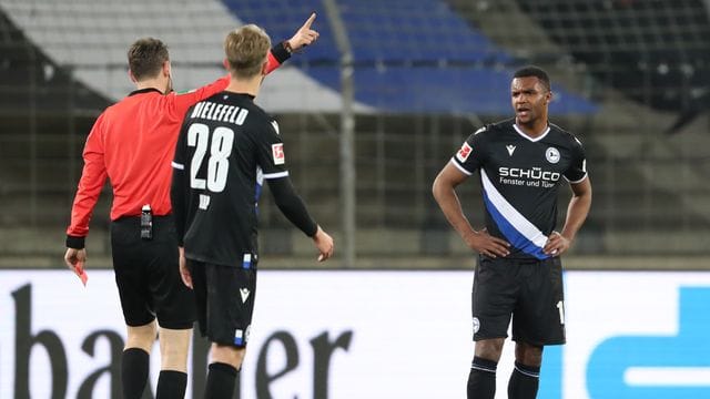 Schiedsrichter Markus Schmidt zeigt Bielefelds Abwehrspieler Nathan de Medina (r) nach der Roten Karte, das Spielfeld zu verlassen.
