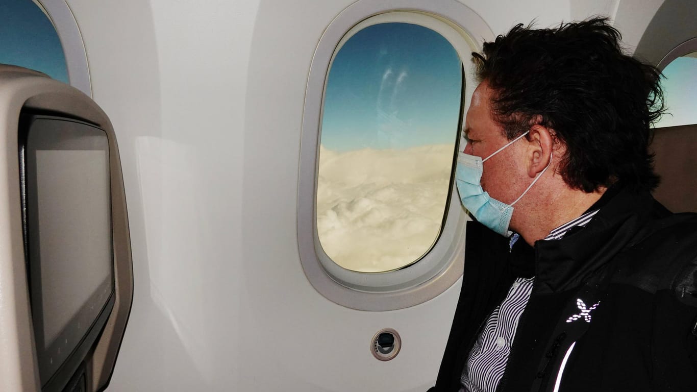 Passagier mit Mund-Nasen-Schutz im Flugzeug: Die Bundesregierung fordert jetzt auf, auf Reisen zu Ostern zu verzichten.