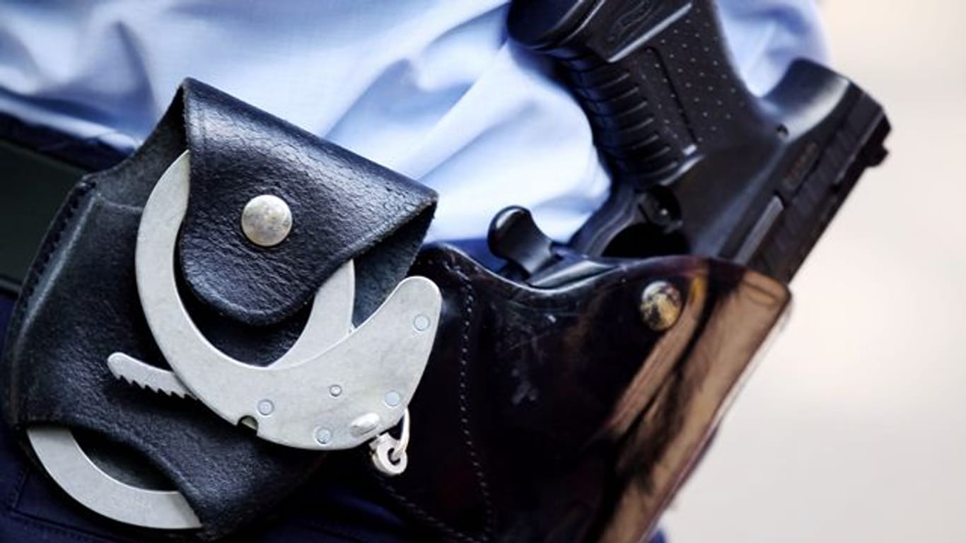 Ein Polizist mit Handschellen und Pistole am Gürtel (Symbolbild): Die Kölner Mordkommission hat nach einer Messerattacke in einem Café zwei Brüder festgenommen.