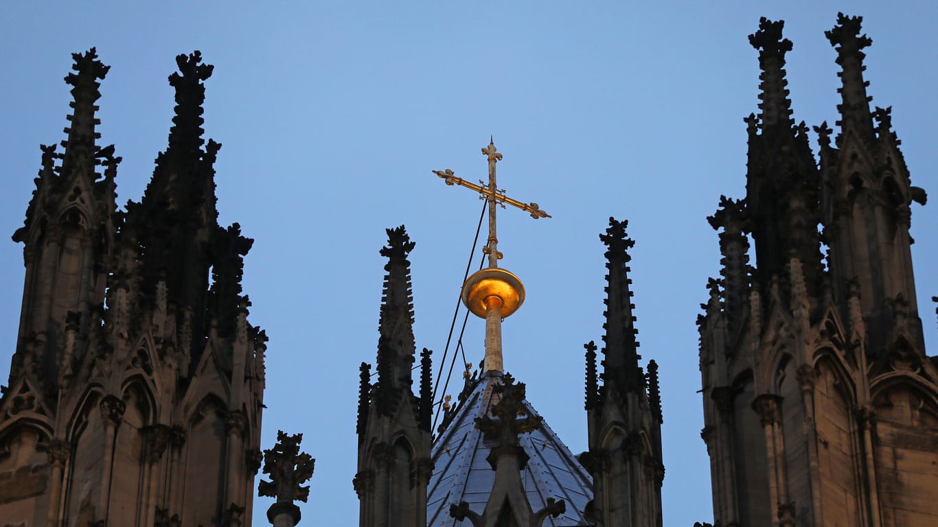Ein Kreuz steht hinter dem Strebewerk am Dom: Das neue Missbrauchsgutachten zum Erzbistum Köln wird am Donnerstag vorgestellt.