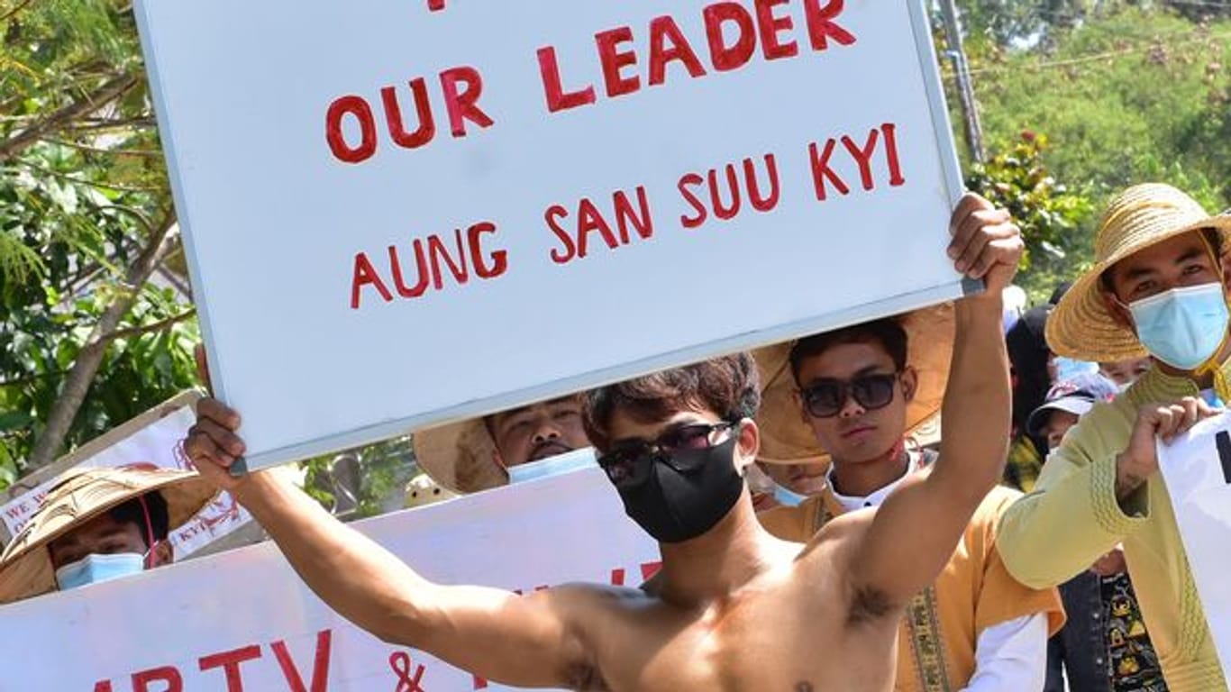 Teilnehmer mit nackten Oberkörpern nehmen an einem Protest teil und halten Schilder mit der Aufschrift "Free our Leader Aung San Suu Kyi" (Befreit unsere Anführerin Aung San Suu Kyi).