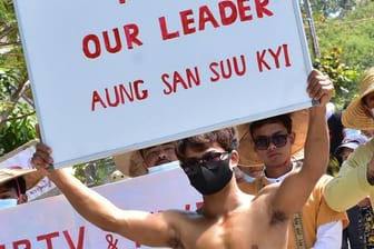 Teilnehmer mit nackten Oberkörpern nehmen an einem Protest teil und halten Schilder mit der Aufschrift "Free our Leader Aung San Suu Kyi" (Befreit unsere Anführerin Aung San Suu Kyi).