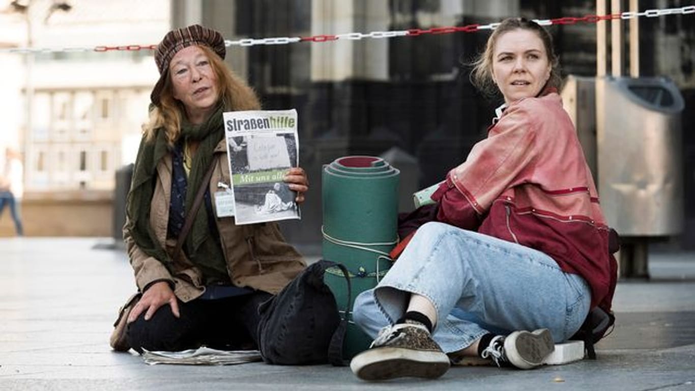 Monika Keller (Rike Eckermann, l) verkauft am Dom Obdachlosenzeitungen.