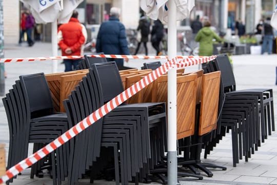 Die Tische und Stühle eines Cafes sind mit Flatterband abgesperrt.