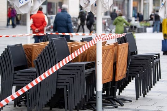 Die Tische und Stühle eines Cafes sind mit Flatterband abgesperrt.