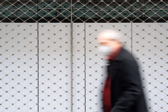 Ein Mann geht in einer Innenstadt an einem geschlossenen Geschäft vorbei.