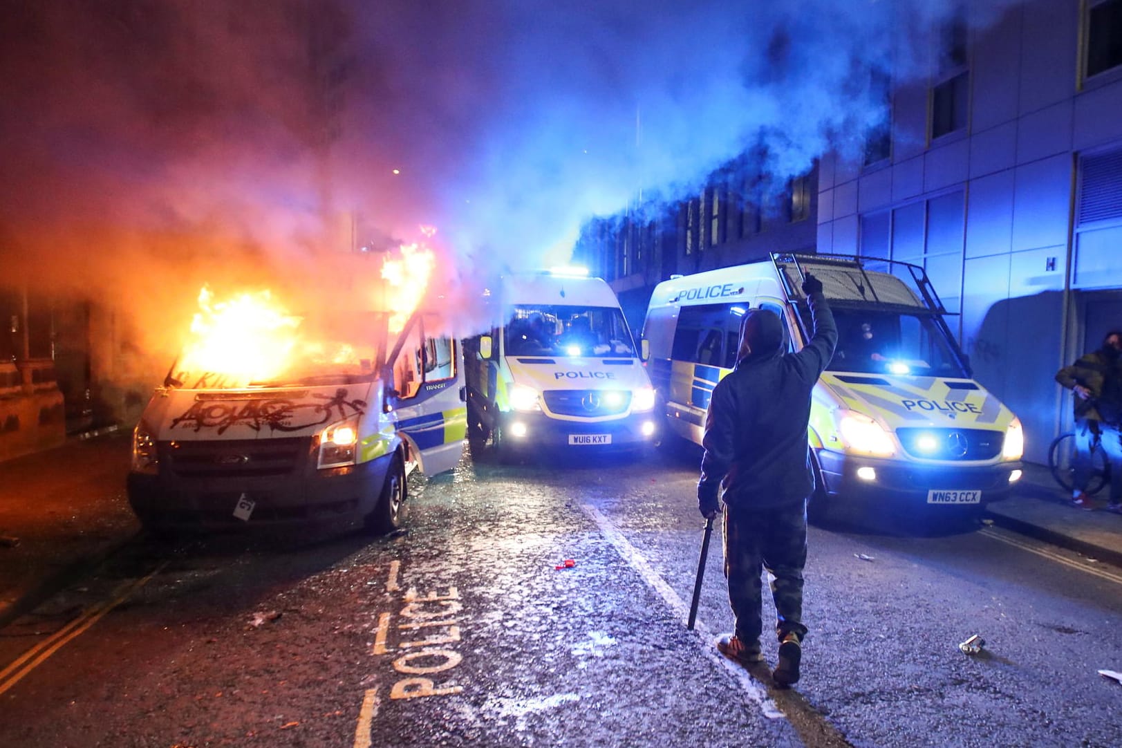 Randalierer in Bristol: Im Hintergrund brennt ein Polizeiauto.