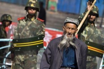 Ein Angehöriger der uigurischen Minderheit in China geht in Ürümqi in der Unruheregion Xinjiang in Nordwestchina vorbei an chinesischen Sicherheitskräften: Die EU hat Strafmaßnahmen beschlossen.