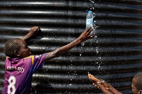 Ein Flüchtlingsjunge aus dem Südsudan fängt in einer Empfangsstelle für Flüchtlinge in Imvepi (Uganda) mit einer Flasche Wasser auf.