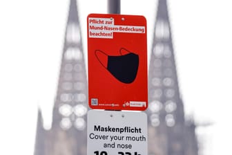 Ein Metallschild weist die Kölner auf die Pflicht zum Tragen einer Mund-Nasen-Bedeckung am Rheinboulevard hin: In Köln ist die Inzidenz seit Tagen über 100.