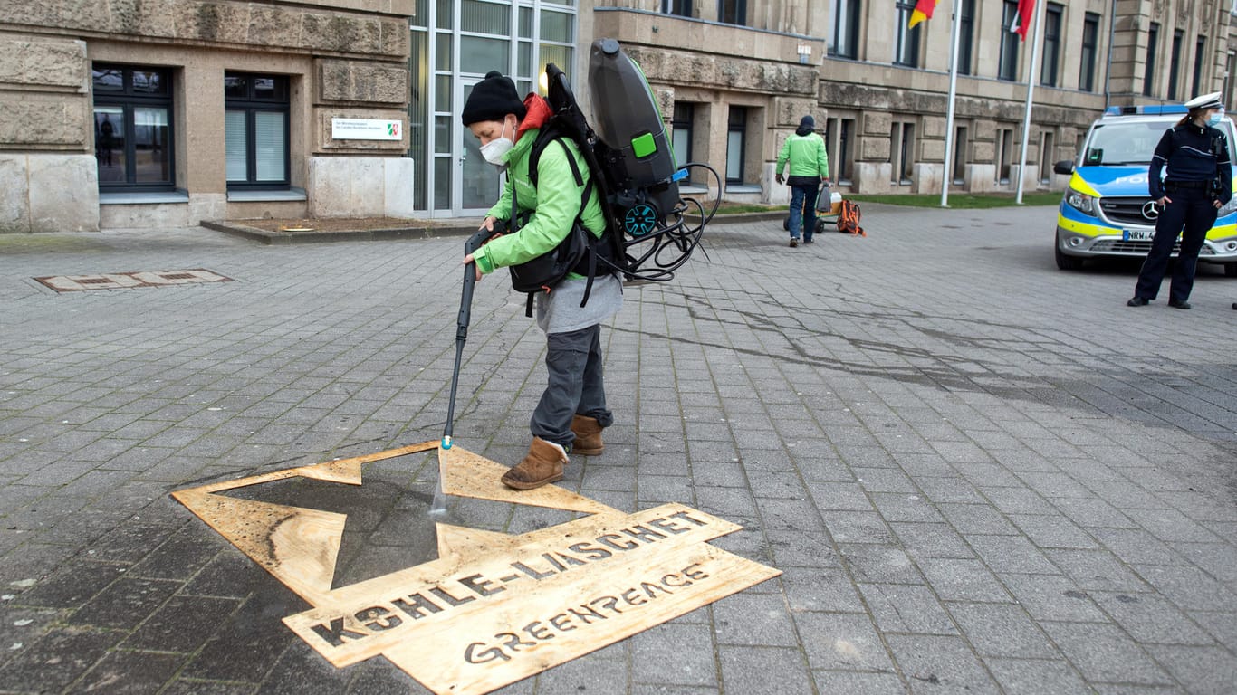 Aktivisten von Greenpeace sprühen mit einer Schablone ein X und "Kohle Laschet" auf das Pflaster am Rheinufer. Greenpeace protestiert damit gegen die Leitentscheidung Braunkohle, die erwartet wird.