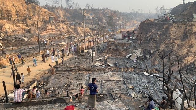 Rohingya-Geflüchtete betrachten nach dem Brand die Überreste des Flüchtlingslager.
