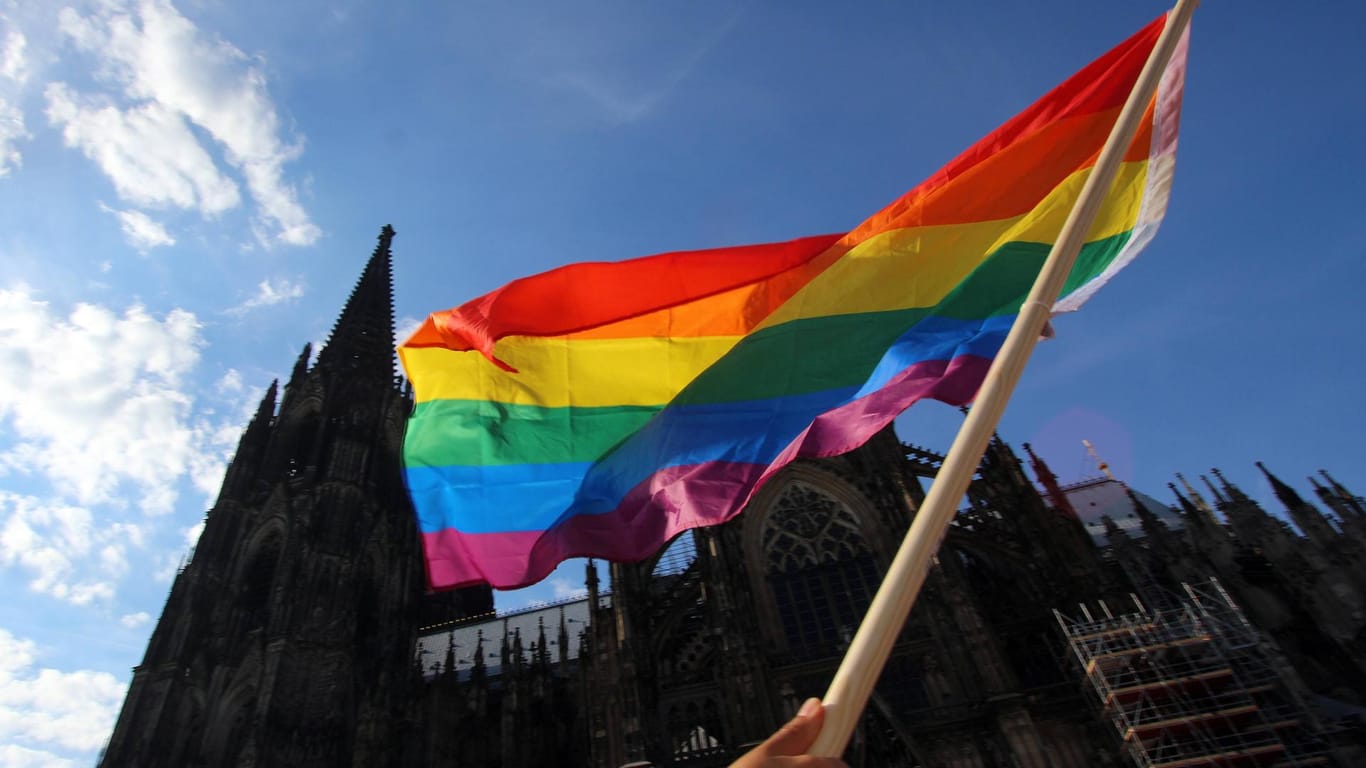 Eine Regenbogenflagge wird vor dem Kölner Dom in die Luft gehalten (Archivbild): Das Bistum Köln stützt das Segnungsverbot für homosexuelle Paare.