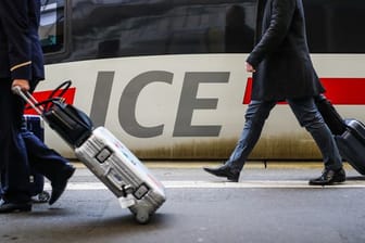 Fahrgäste gehen mit ihrem Gepäck an einem ICE-Zug vorbei.
