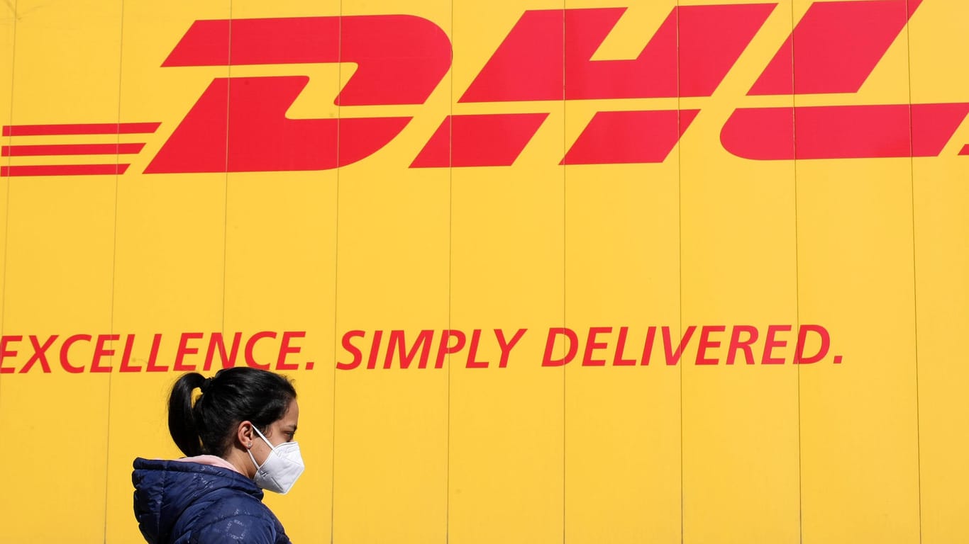 Eine Frau mit Schutzmaske vor einem DHL-Logo (Symbolbild): Künftig sollen Kunden des Paketdiensts schneller an ihr Paket kommen.