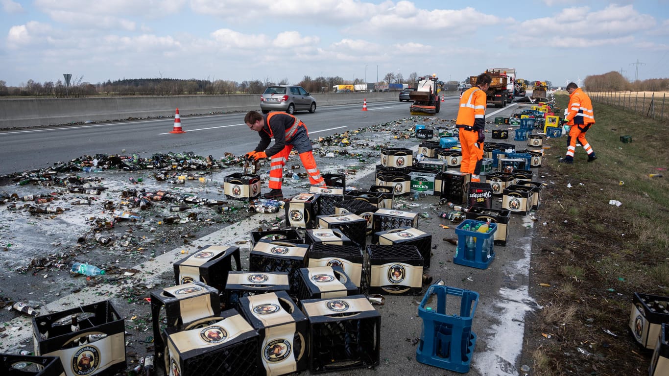 Etliche zerstörte Bierflaschen liegen nach einem Unfall mit einem Getränkelaster auf der Autobahn 7: Mitarbeiter der Straßenmeisterei reinigen die Fahrbahn.