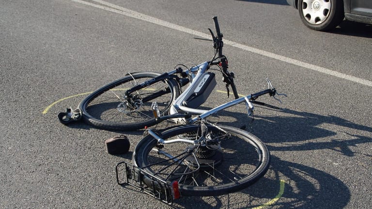 Ein Fahrrad liegt nach einem Unfall auf der Straße (Symbolbild): In Köln hat eine Autofahrerin einen Radfahrer beim Überqueren einer Kreuzung erfasst.