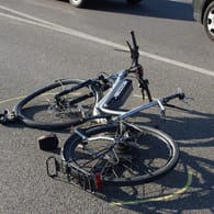 Ein Fahrrad liegt nach einem Unfall auf der Straße (Symbolbild): In Köln hat eine Autofahrerin einen Radfahrer beim Überqueren einer Kreuzung erfasst.