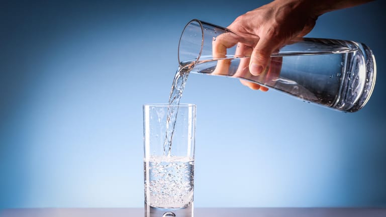 Mann schenkt sich ein Glas Wasser ein: Mineralwasser kann, wenn es bewusst ausgewählt ist, gegen Osteoporose vorbeugen