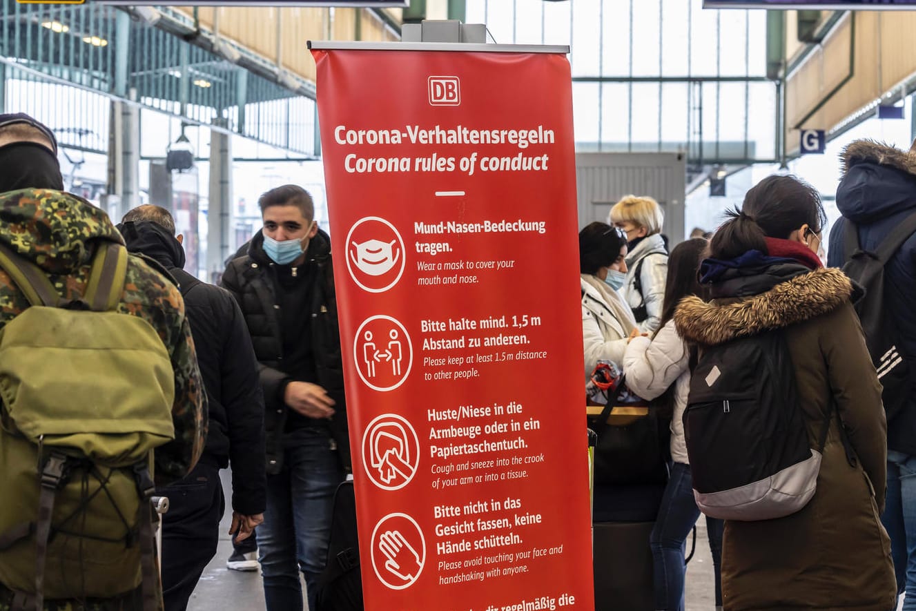 Reisende am Hauptbahnhof Stuttgart: Ein Schild verweist auf die Corona-Verhaltensregeln.