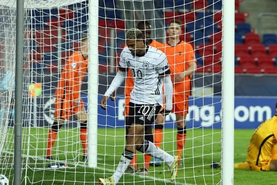 Deutschlands Lukas Nmecha (M) holt nach seinem Tor zum 1:1 den Ball aus dem Tor - der niederländische Torwart Kjell Scherpen (r) sitzt geschlagen auf dem Rasen.