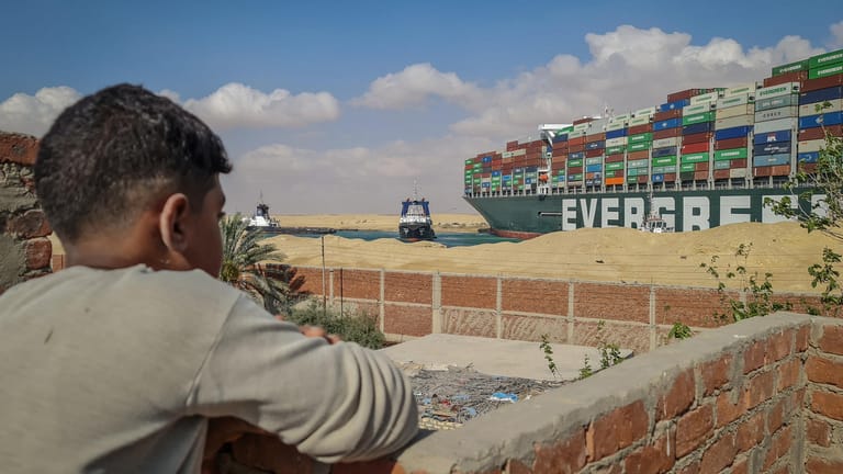 Ein Junge schaut auf das feststeckende Containerschiff im Suezkanal. Durch die Blockierung kommen auch Frachter mit Schafen nicht weiter.