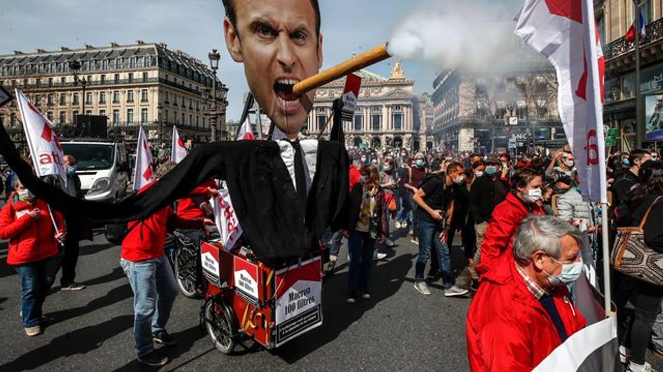 Demonstranten ziehen mit einem Zigarre rauchenden Abbild des französischen Präsidenten Macron durch Paris.