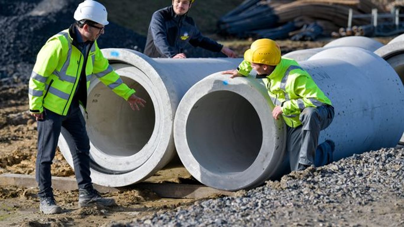 Shenadi Osmani bespricht mit den angehenden Kanalbauern Issam Bhihi und Steffen Hallermann die Kontrolle der Dichtungen von Betonrohren auf einer Baustelle.