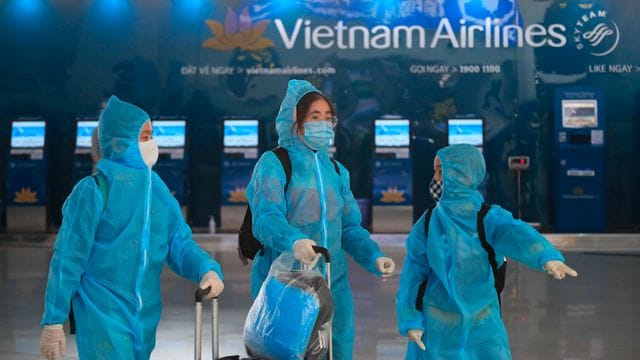 Passagiere in voller Schutzkleidung gegen das Coronavirus gehen durch den Flughafen Hanoi. Passagiere in voller Schutzkleidung gegen das Coronavirus gehen durch den Flughafen Hanoi.