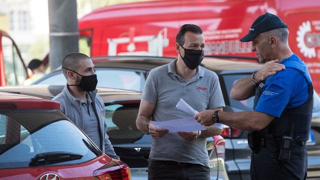 Zwei Männer sprechen am Grenzübergang mit einem Grenzbeamten und zeigen Dokumente vor.