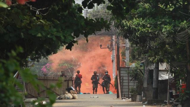 Uniformierte Soldaten mit Gewehren gehen in Yongon während einer Demonstration von Anti-Putsch-Demonstranten auf eine Rauchwolke zu. Uniformierte Soldaten mit Gewehren gehen in Yongon während einer Demonstration von Anti-Putsch-Demonstranten auf eine Rauchwolke zu.