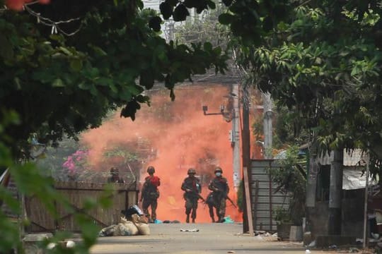 Uniformierte Soldaten mit Gewehren gehen in Yongon während einer Demonstration von Anti-Putsch-Demonstranten auf eine Rauchwolke zu.