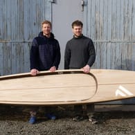 Michael Walther, Jannek Grocholl halten das besondere SUP in den Händen. Für die Produktion aus besonderem Holz entsteht eine eigene Plantage.