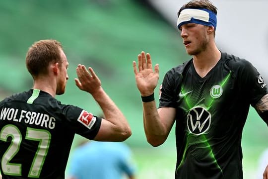 Wolfsburgs Stürmer Weghorst (r), der einen Verband am Kopf trägt, bejubelt einen Treffer mit Mannschaftskamerad Arnold.