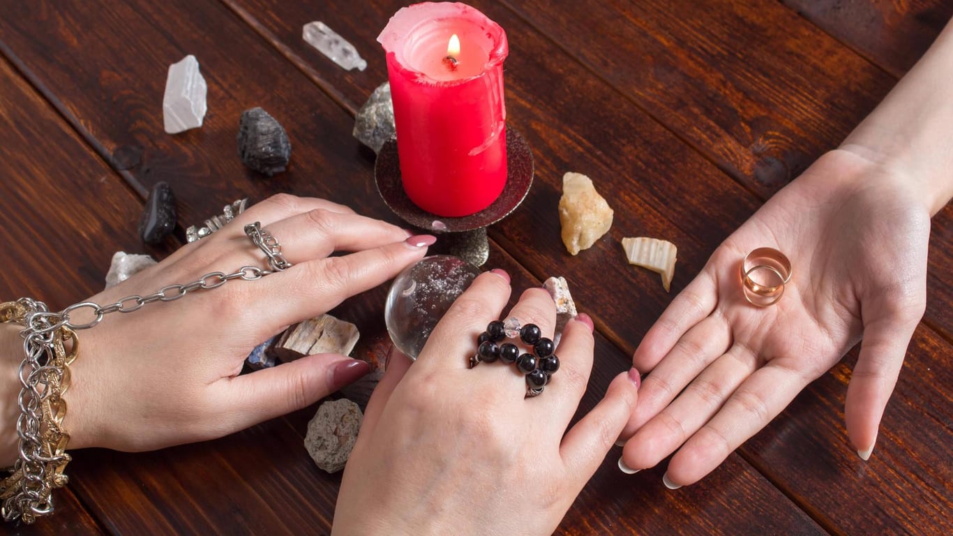Hände und Steine liegen um eine Kerze (Symbolbild): Eine "Wahrsagerin" hat ihre Kunden um mehr als 100.000 Euro betrogen.