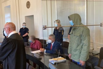 Zwei Angeklagte (3.v.l und r) in einem Prozess um einen mutmaßlichen Mord sitzen und stehen in einem Gerichtsaal: Einer der beiden Brüder soll einen Mann vor einen einfahrenden Zug gestoßen haben.