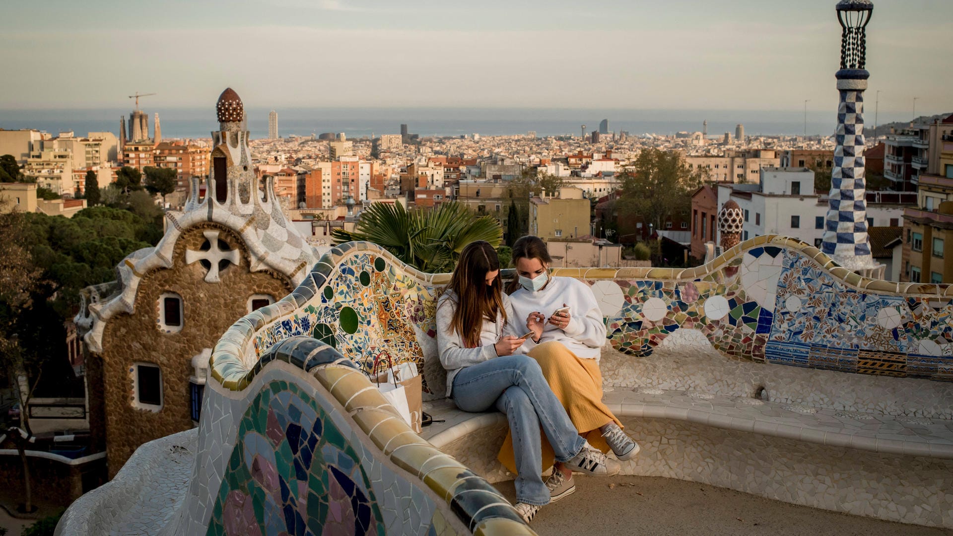 Barcelona: Zwei Mädchen sitzen auf einer Bank und tragen Masken. Die Stadt war zwischenzeitlich besonders von der Pandemie getroffen.