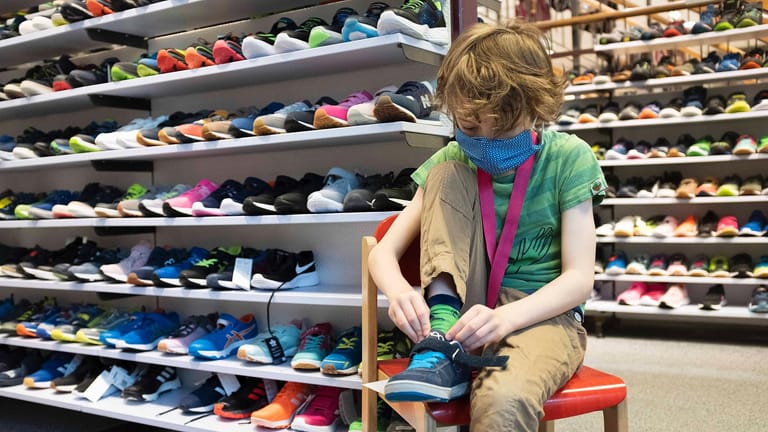 Junge probiert Schuhe an (Archivbild): In Bayern dürfen die Schuhgeschäfte laut einem Urteil wieder öffnen – denn gerade Kinder und Jugendliche könnten sehr schnell neues Schuhwerk brauchen.
