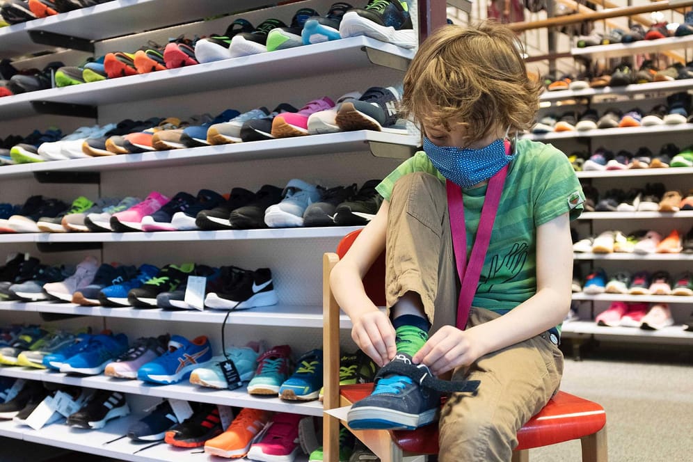 Junge probiert Schuhe an (Archivbild): In Bayern dürfen die Schuhgeschäfte laut einem Urteil wieder öffnen – denn gerade Kinder und Jugendliche könnten sehr schnell neues Schuhwerk brauchen.