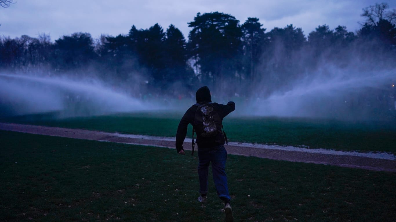 Ein Teilnehmer der illegalen Party in Brüssel steht am Freitagabend vor den Strahlen zweier Wasserwerfer.